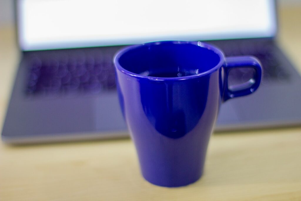 Bildet viser en blå kopp foran en Apple Mac bærbar PC og er ment å visualisere arbeid på nettet for å komme høyt opp i Google på nettstedet OMACO AS