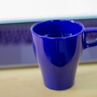 Bildet viser en blå kopp foran en Apple Mac bærbar PC og er ment å visualisere arbeid på nettet for å komme høyt opp i Google på nettstedet OMACO AS